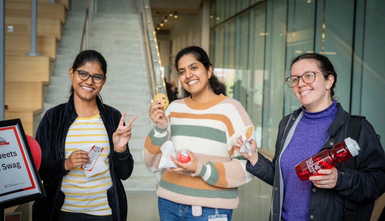 Three smiling students stand together, posing with cookies and swag.