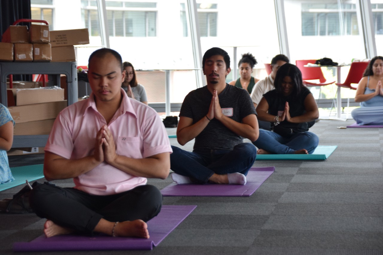 Graduate students sit in the lotus pose on yoga mats.